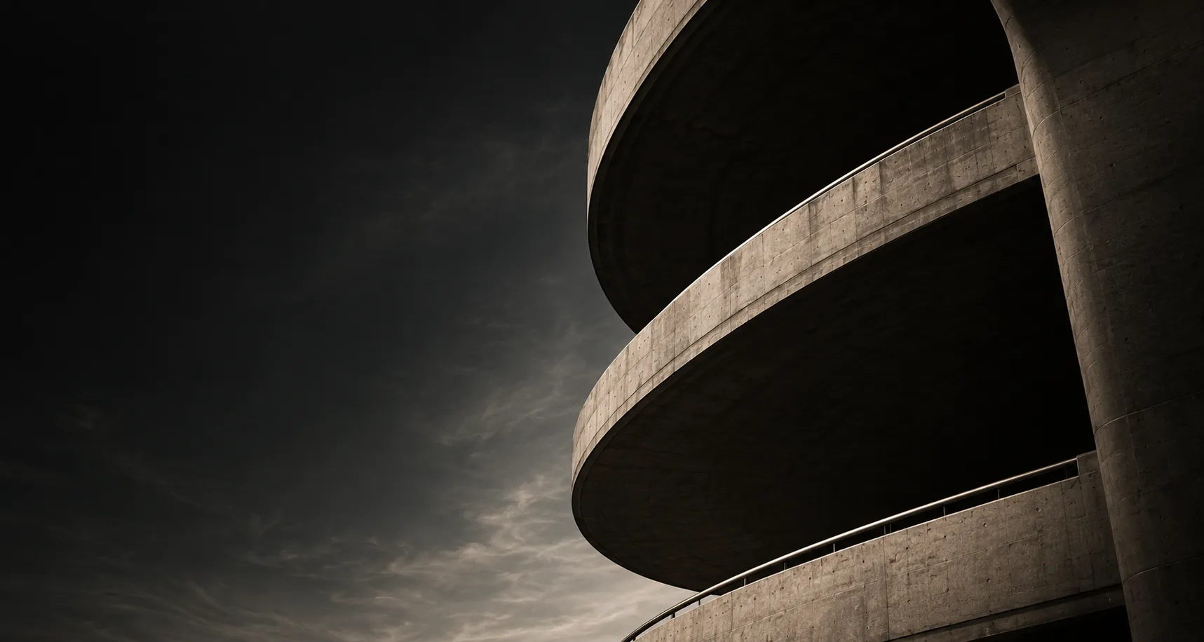 Curved concrete ramps of a brutalist car park against a dark sky.